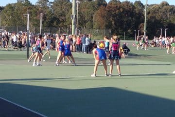 Several teams in blue and red netball uniforms competing in a match on an outdoor court