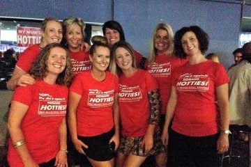 A group of seven smiling women posing together while wearing matching red t-shirts that celebrate "Hogans Hotties" as the 2015 Grand Final Winners.