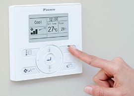 Home » Hot water system A close-up of a person's finger pressing a button on a white, wall-mounted Daikin digital thermostat display.