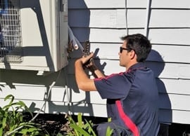Home » Hot water system A technician in a dark blue polo with red stripes crouching while installing or repairing the external connections of an outdoor air conditioning unit