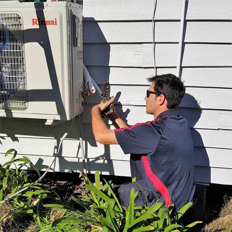 A technician in a navy blue polo with red stripes kneeling while using a flaring tool on copper piping for a Rinnai air conditioning unit