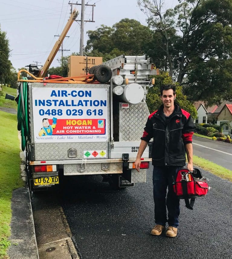 Jamie carrying a red tool bag stands next to a service truck loaded with equipment