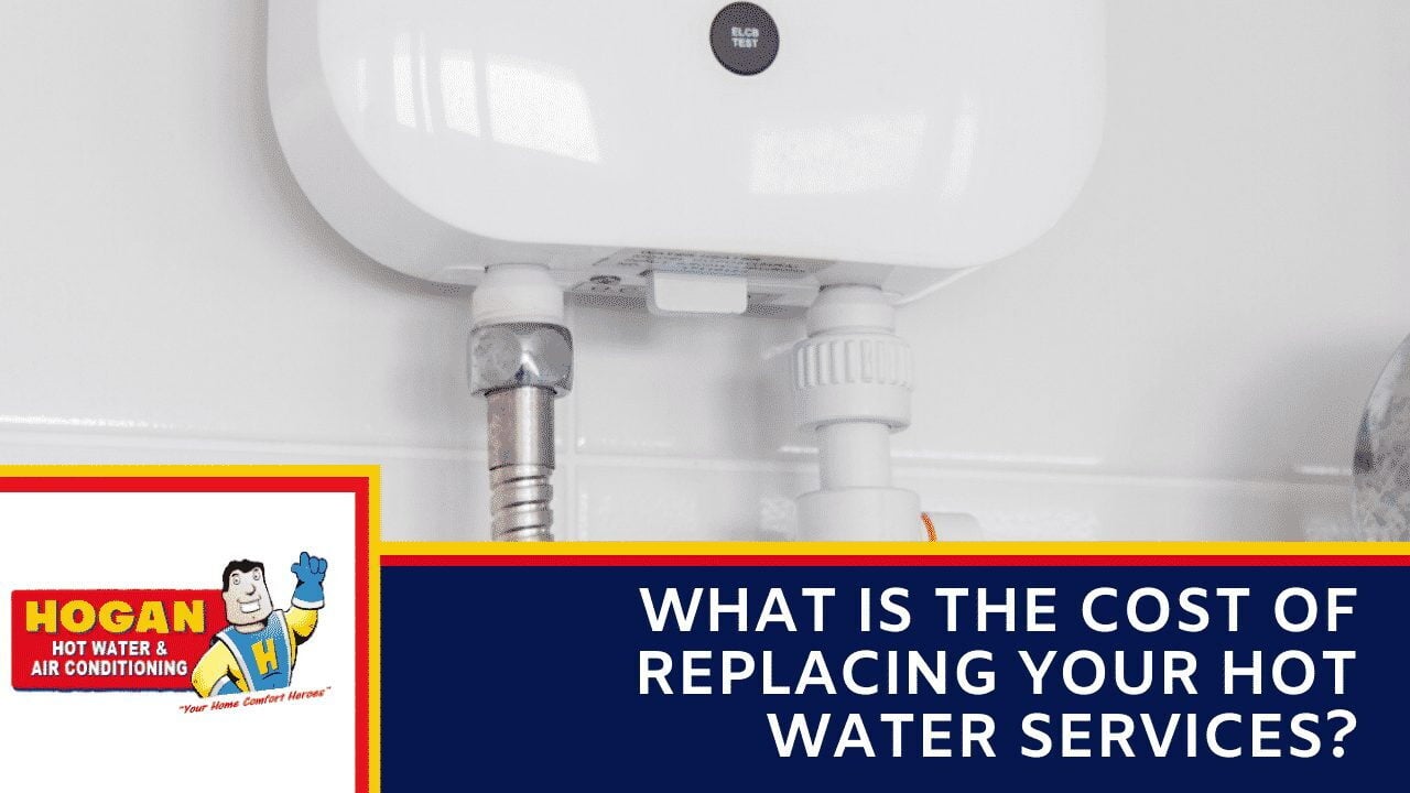 A white electric hot water unit with plumbing connections mounted on a white tiled wall.