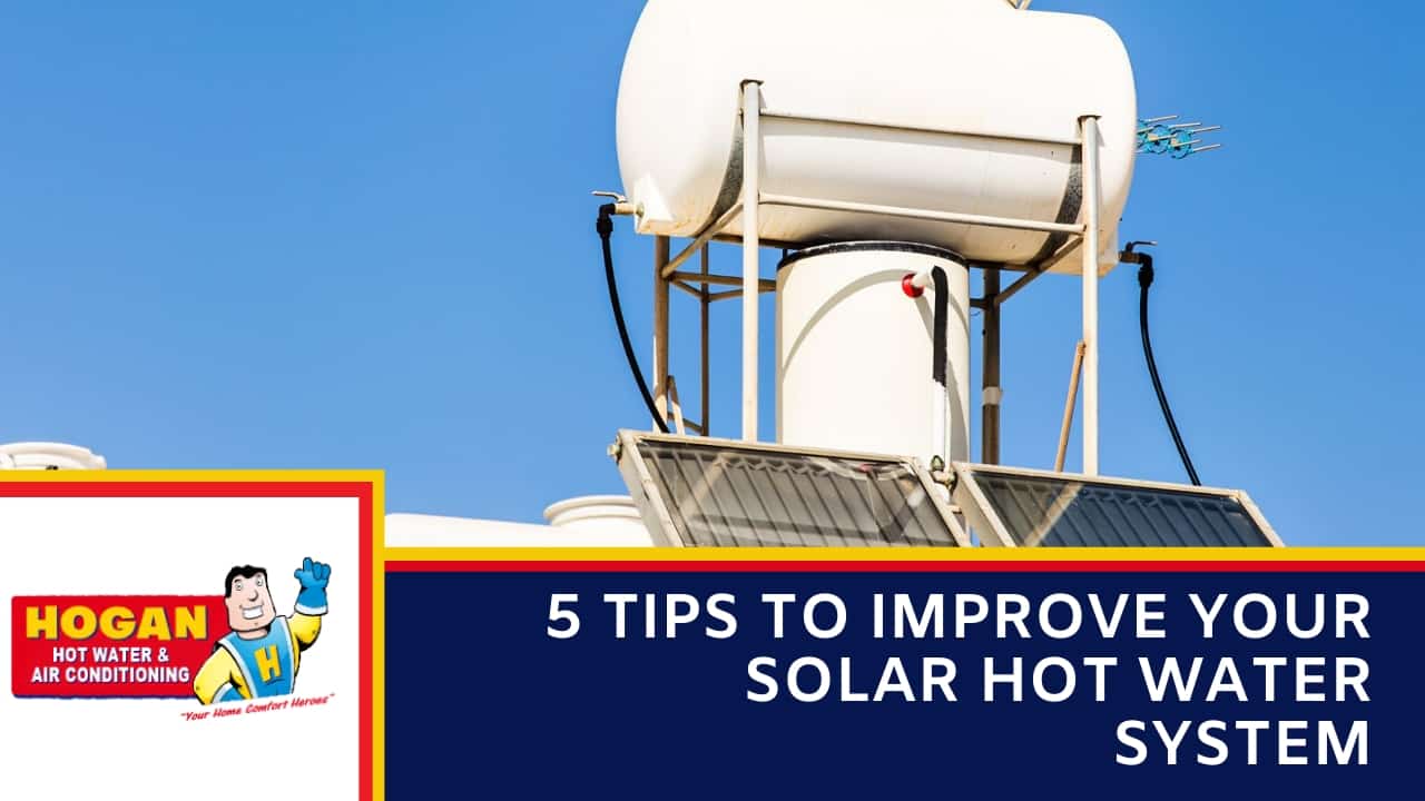 A white rooftop solar hot water unit with a large storage tank and collector panels against a clear blue sky.