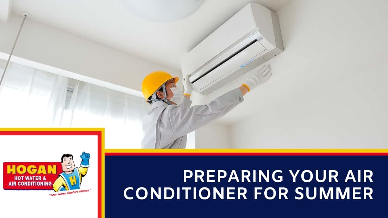 A technician in a yellow hard hat, face mask, and gloves inspecting a white split-system air conditioning unit