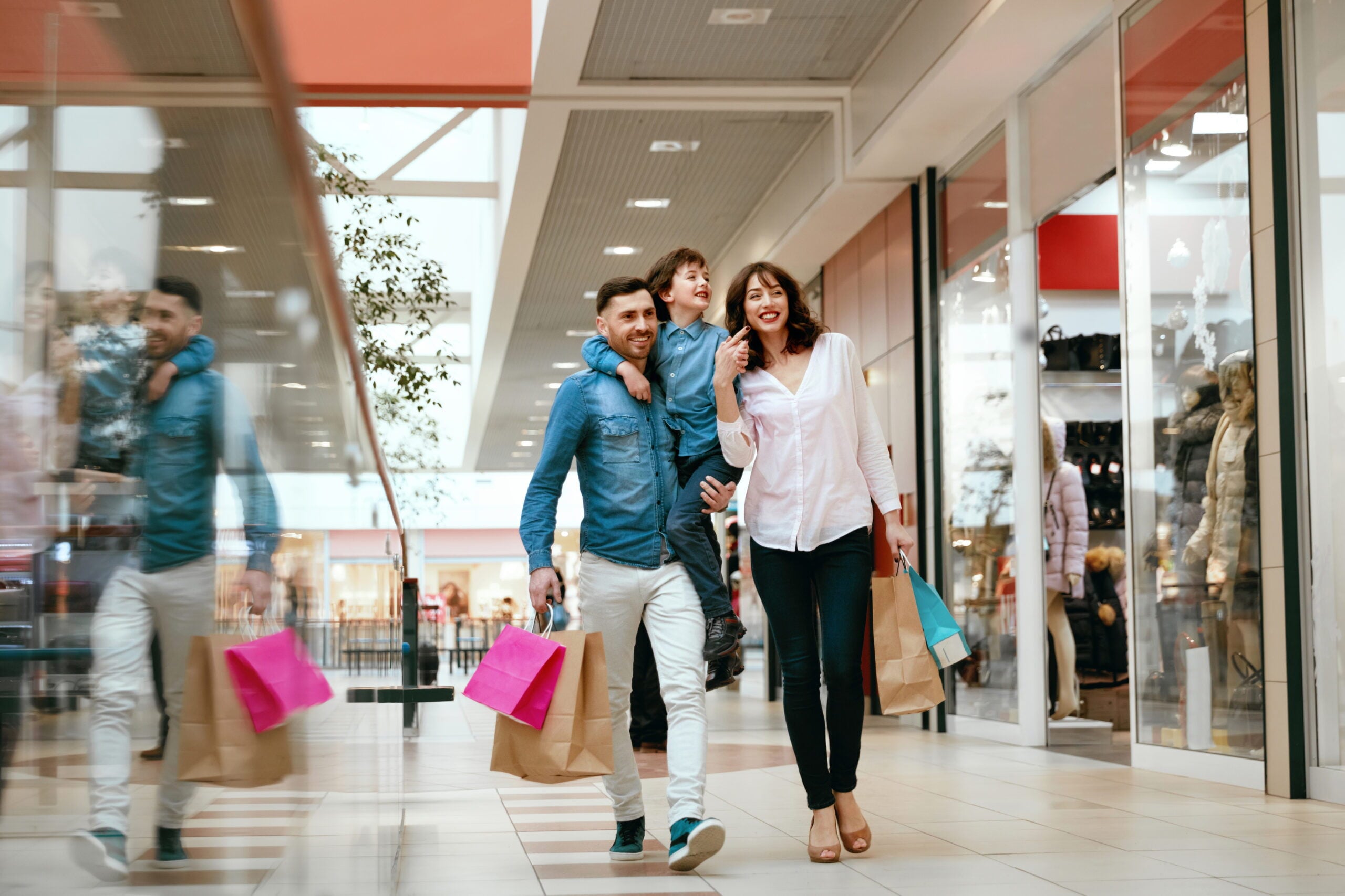 A happy family of three walking through a bright, modern shopping mall