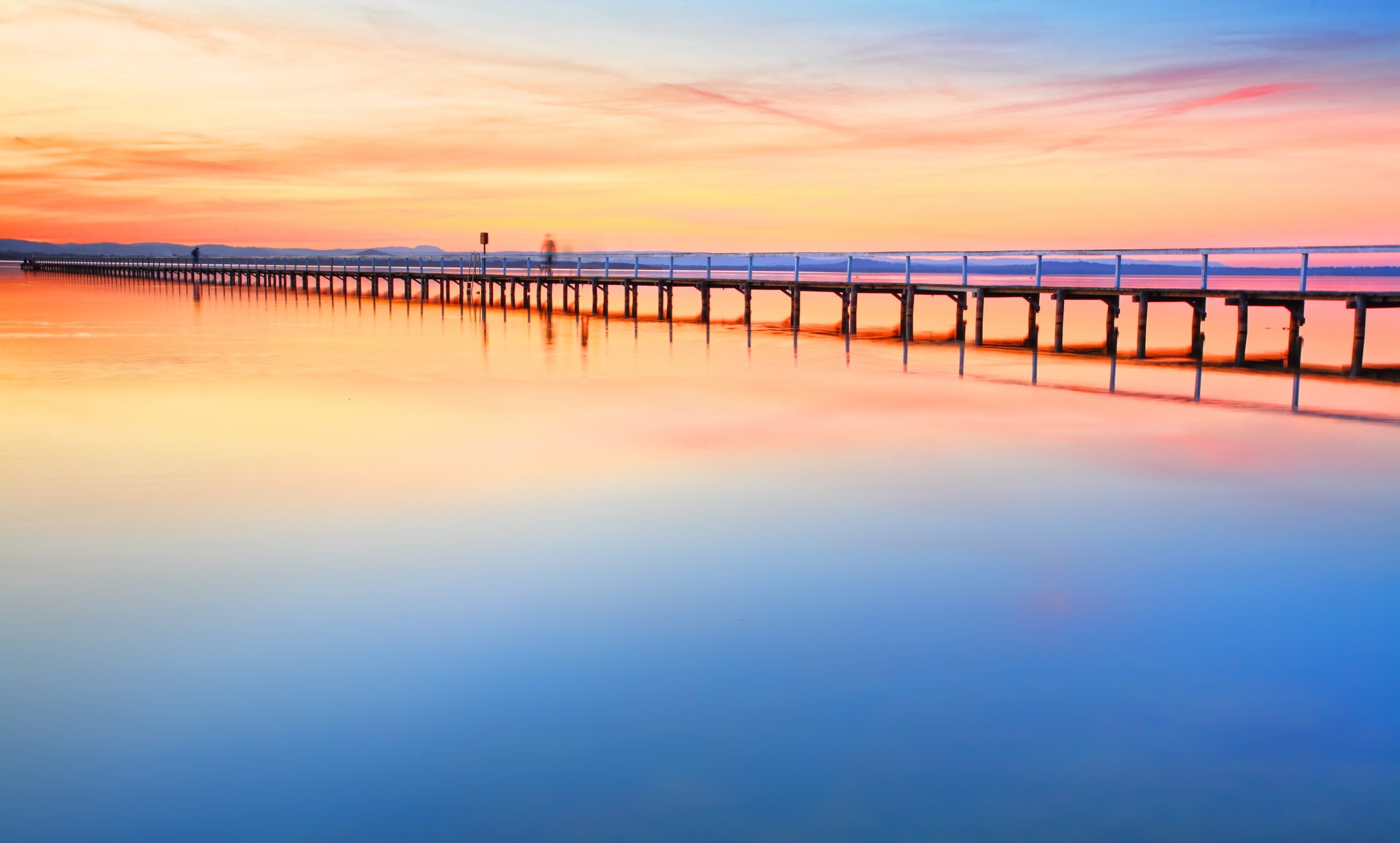 A long wooden pier stretching across a calm lake at sunset