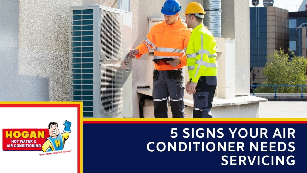 A two technicians in high-visibility gear and hard hats inspecting a large rooftop air conditioning unit.
