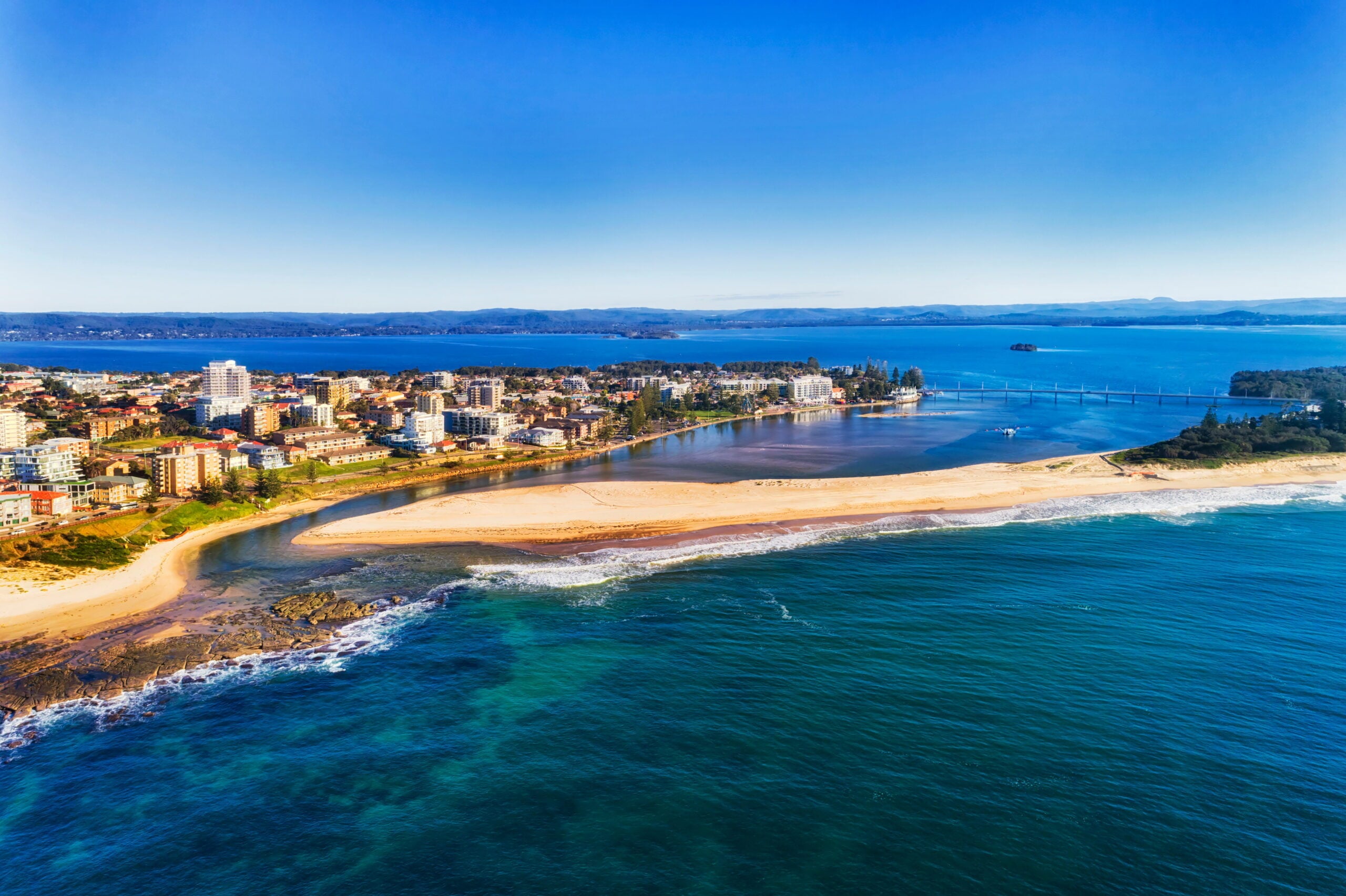 A vibrant coastal city where a turquoise ocean meets a calm blue lagoon in Tuggerah