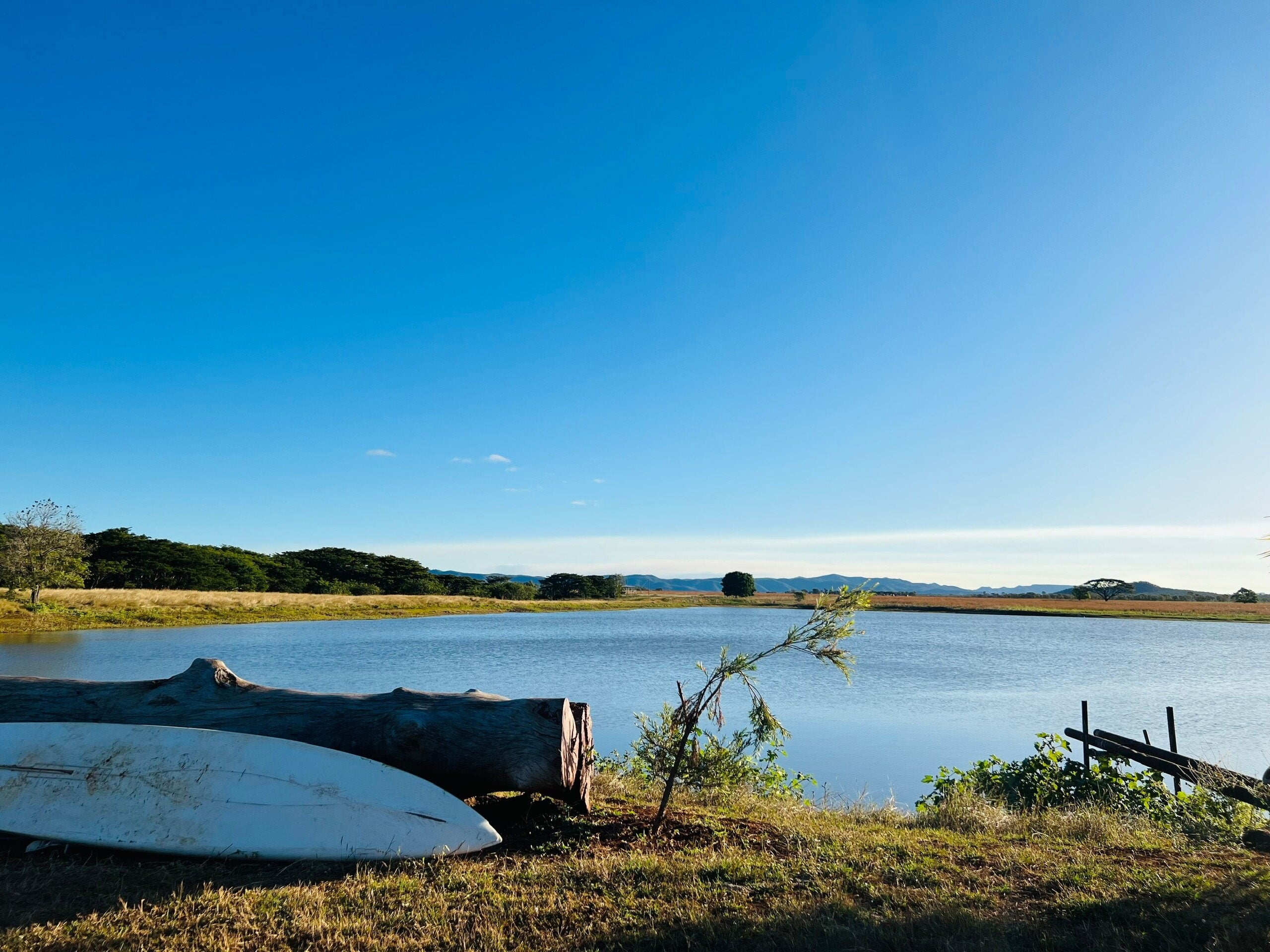 A calm lake or river landscape under a vast blue sky.