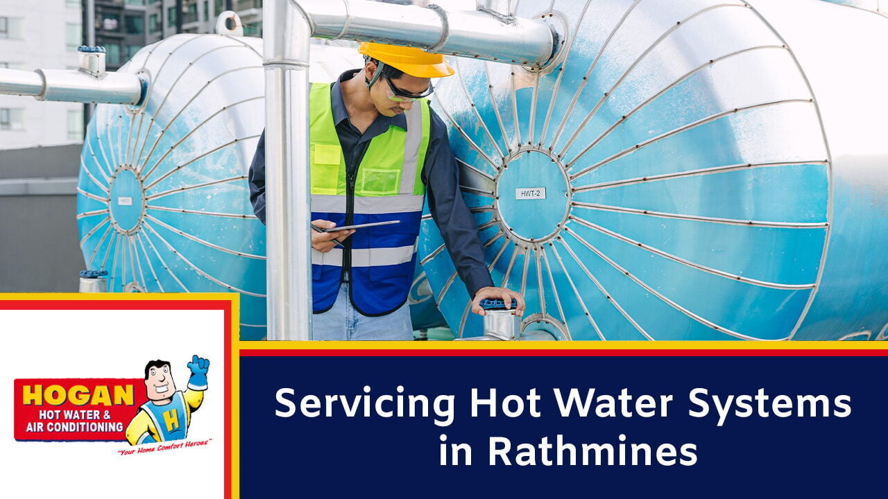 A technician in a yellow hard hat and safety vest inspects large industrial water tanks.