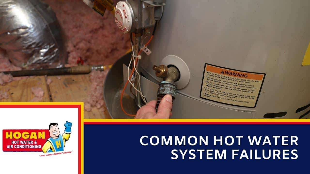 A hand attaching a drainage hose to the brass valve of a hot water storage tank
