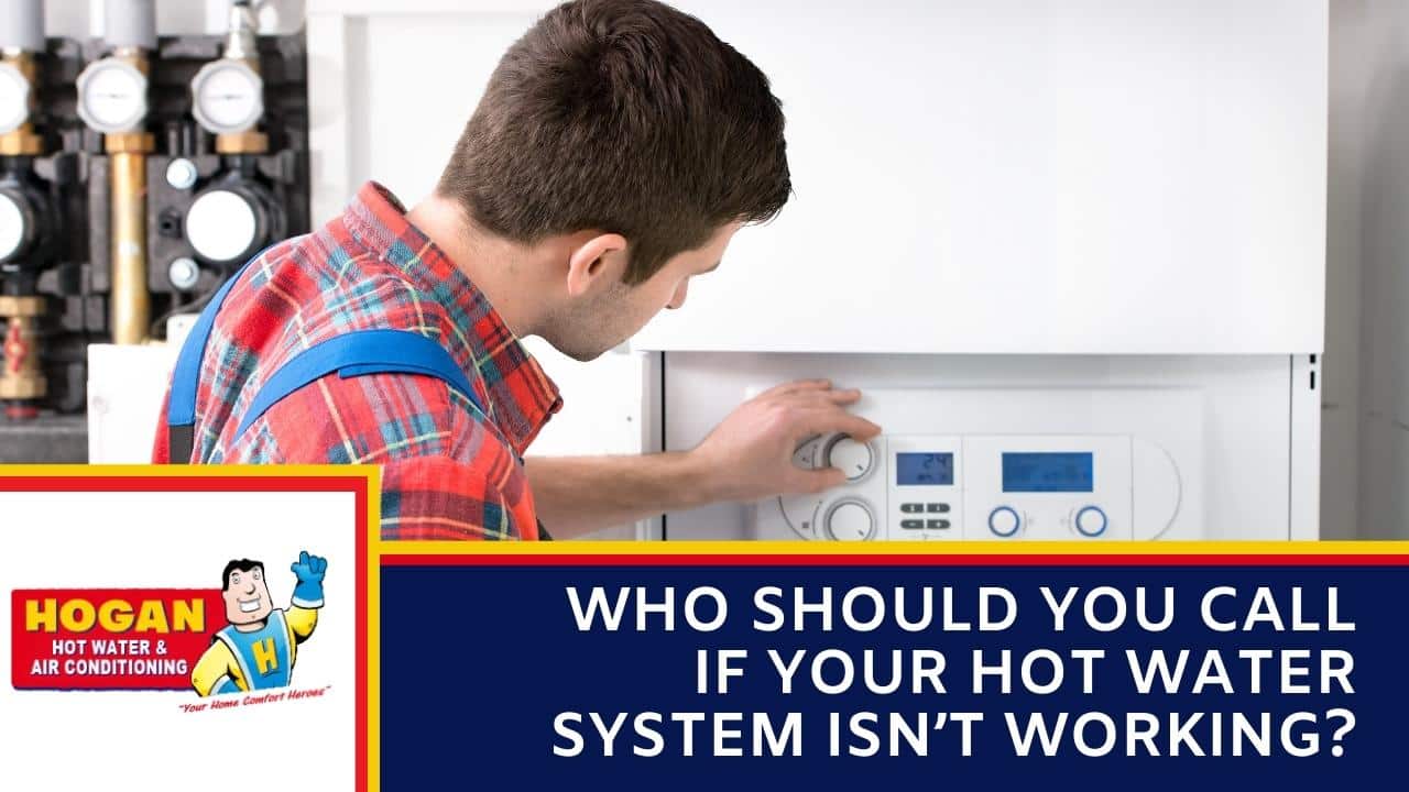 A technician in a red plaid shirt and blue overalls adjusting a dial on the white control panel of a wall-mounted boiler system.