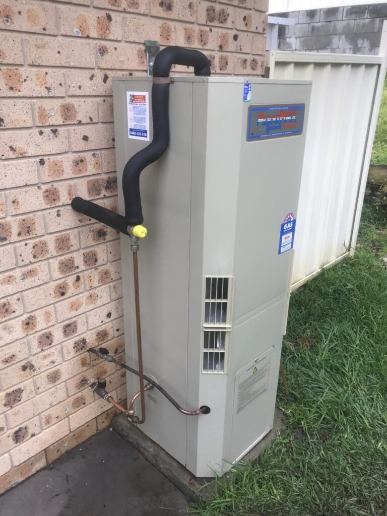 An AquaMax gas hot water system installed against an exterior brick wall.
