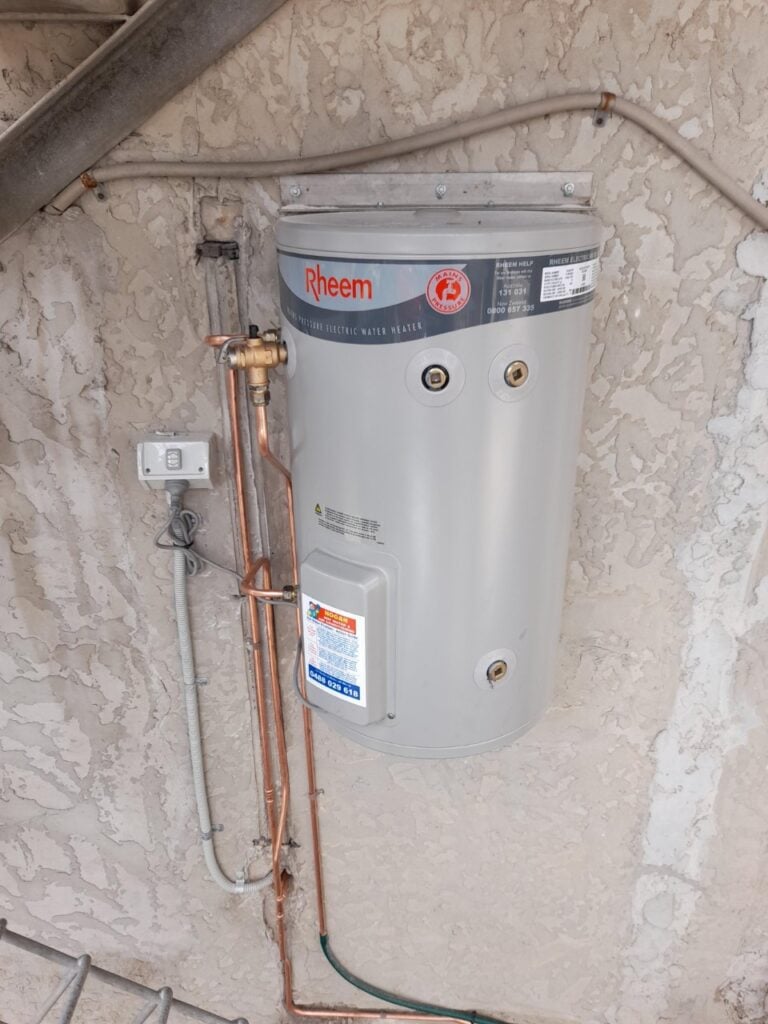 Wall-mounted Rheem electric water heater with copper piping mounted on a concrete wall.