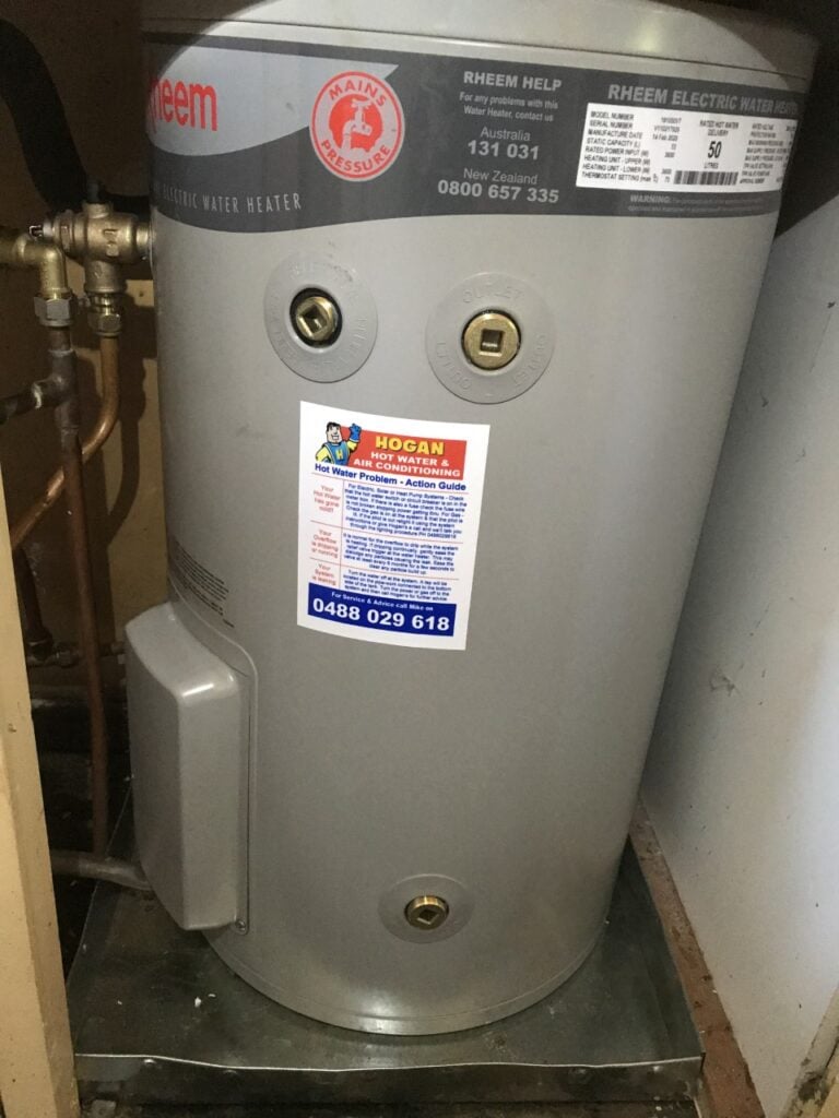 Compact Rheem indoor electric water heater installed inside a narrow cupboard or utility space.
