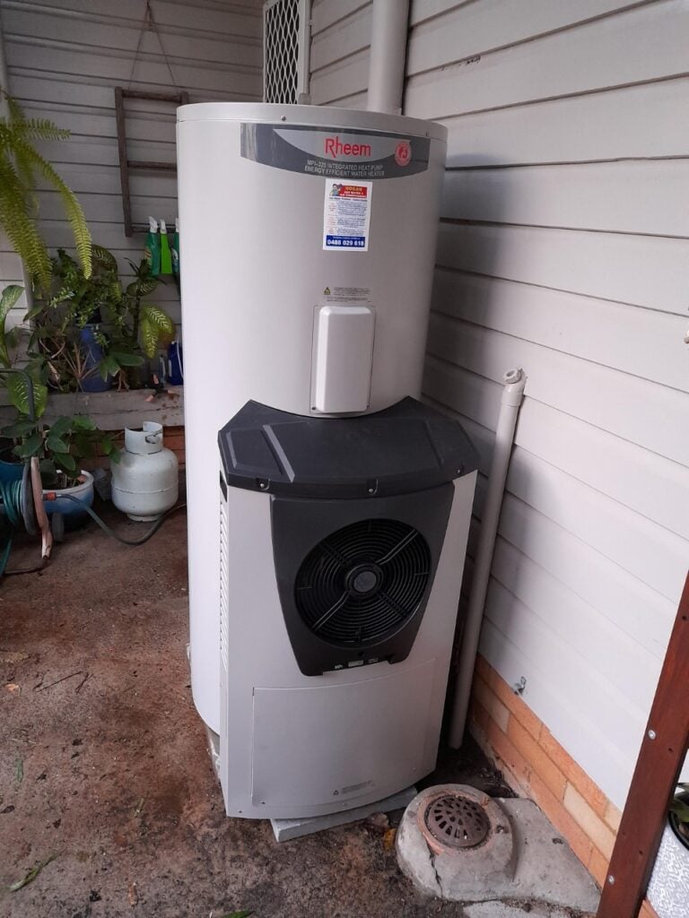 A Rheem integrated heat pump hot water system installed outdoors against a house wall.