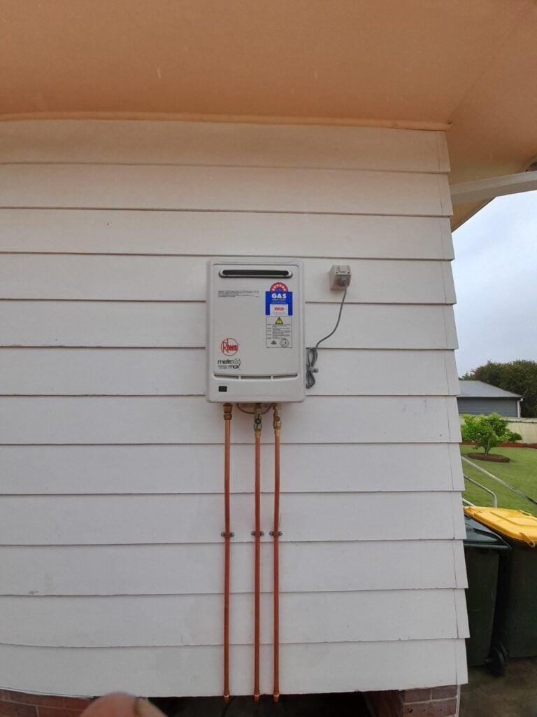 Wall-mounted Rheem Metro continuous flow gas hot water unit mounted on white weatherboard siding.