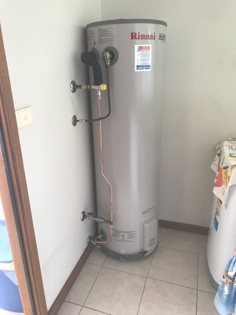 Indoor Rinnai electric water heater tank installed in a tiled laundry room corner.