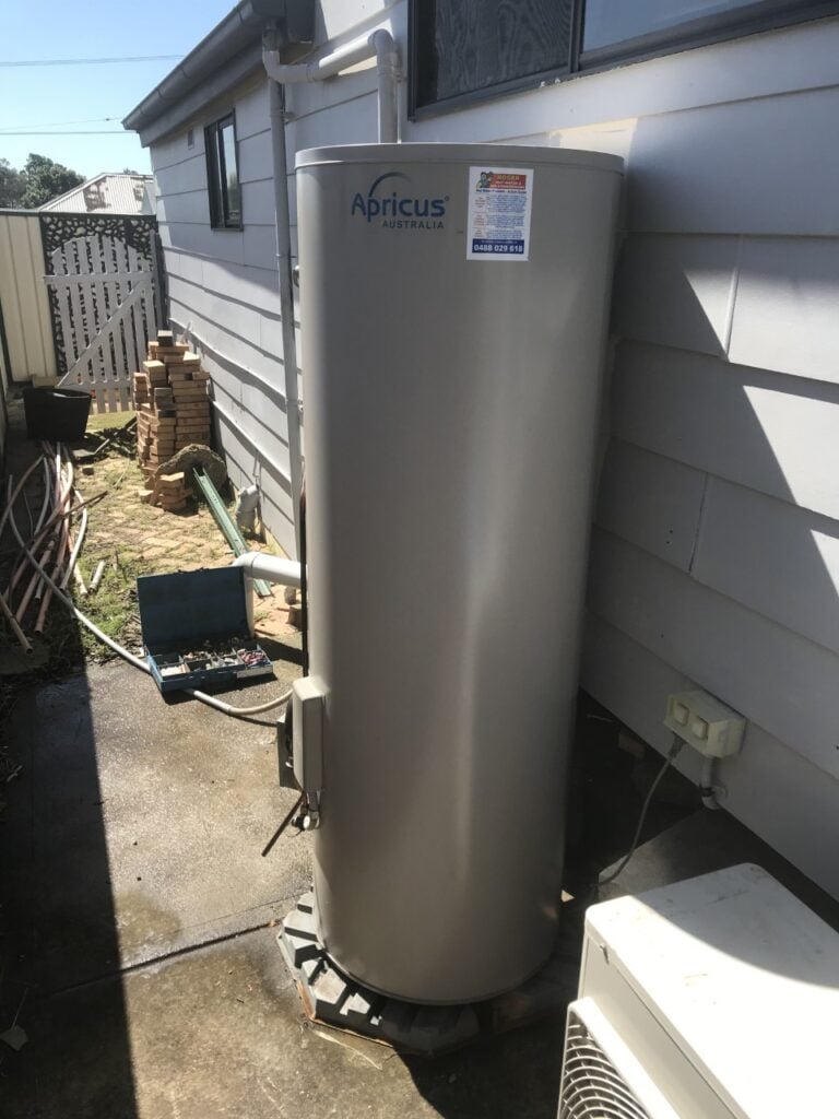 An Apricus Australia hot water storage tank installed outdoors in a narrow concrete side walkway.