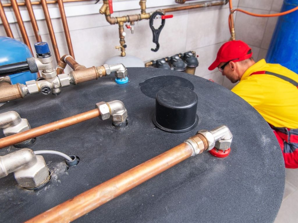 A high-angle view focusing on the copper pipe connections on top of a black cylindrical water heater tank.