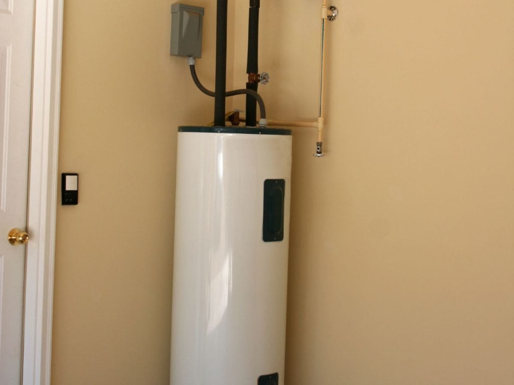 A wide view of a tall, white cylindrical electric hot water storage tank.