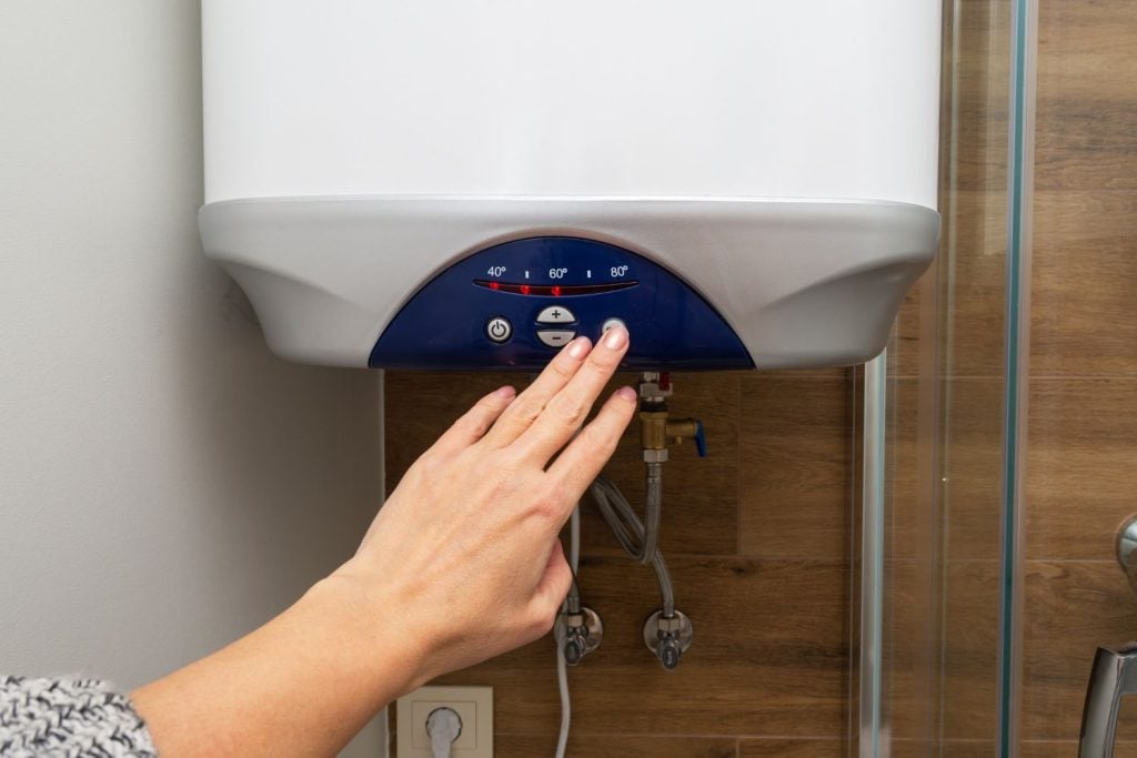 Hot Water Installation and Maintenance Carrington » Carrington A person's hand adjusts the control panel of a white electric water heater, which features temperature settings for 40°C, 60°C, and 80°C.