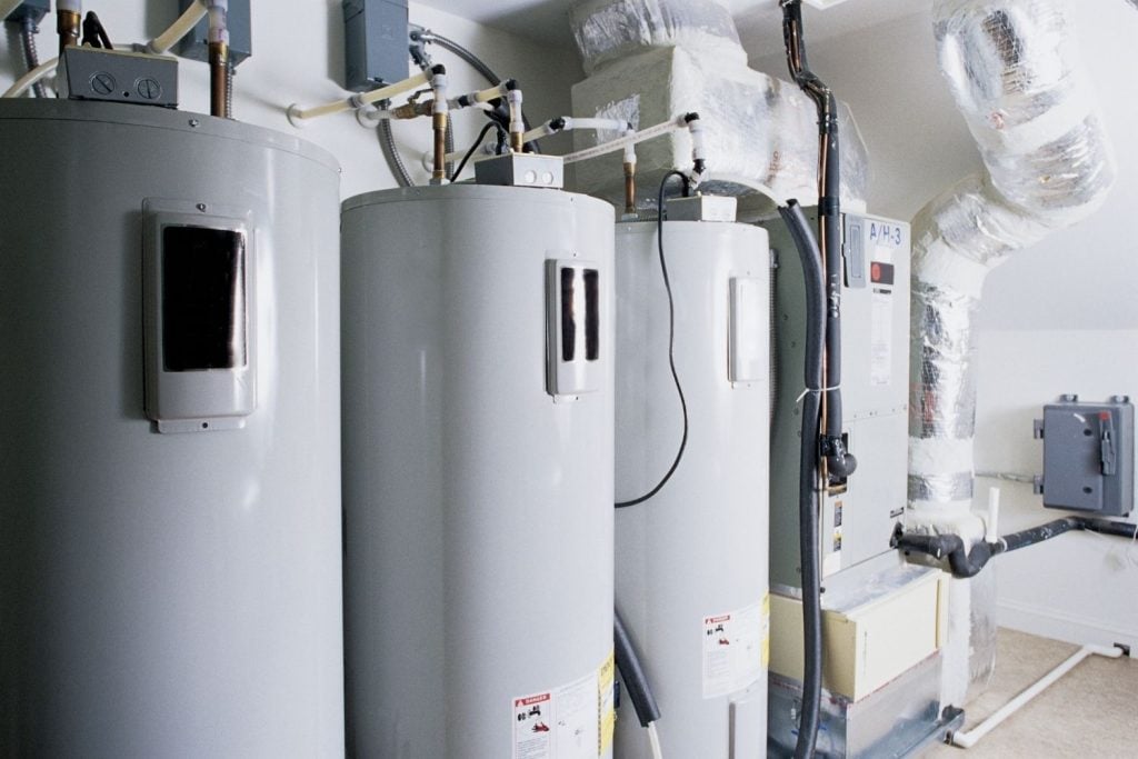 Hot Water Installation and Maintenance Beresfield » Beresfield An interior view of a utility room or basement showing a row of three large, grey electric water heaters.