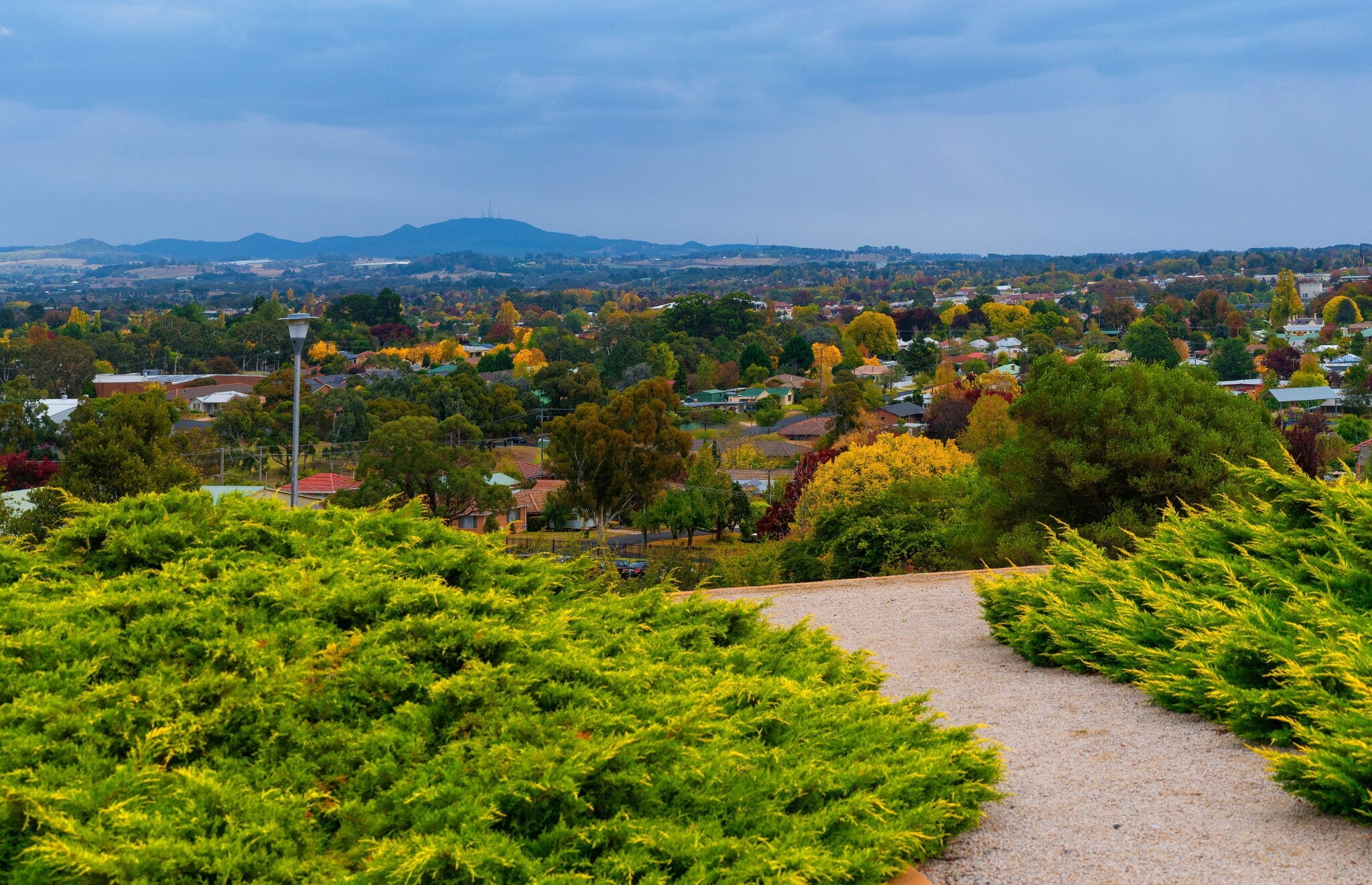 A gravel path overlooking a sprawling town with autumn trees and mountains in the distance.