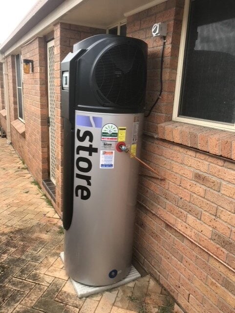An outdoor iStore heat pump hot water system with a silver tank and black compressor unit.