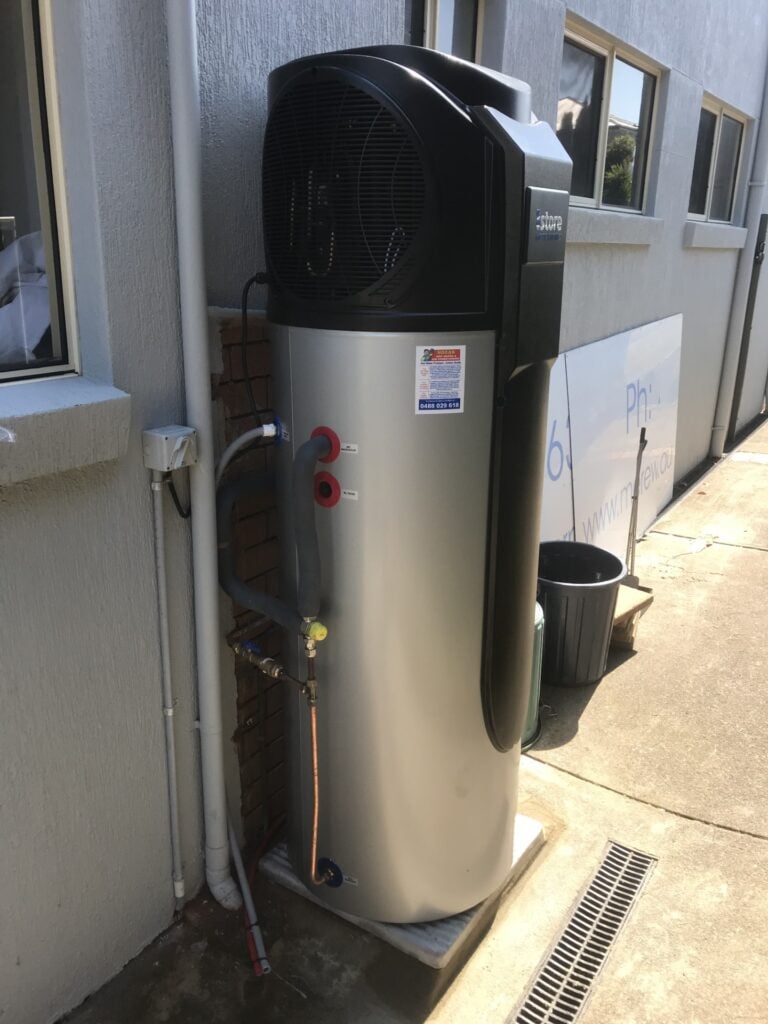 An outdoor iStore heat pump hot water system with a tall silver tank and black compressor unit installed on a concrete base