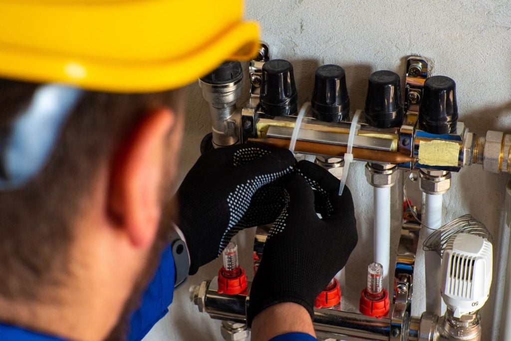 Hot Water Installation and Maintenance Jesmond » Jesmond A technician wearing a yellow hard hat and black work gloves secures components of a manifold system with white zip ties.