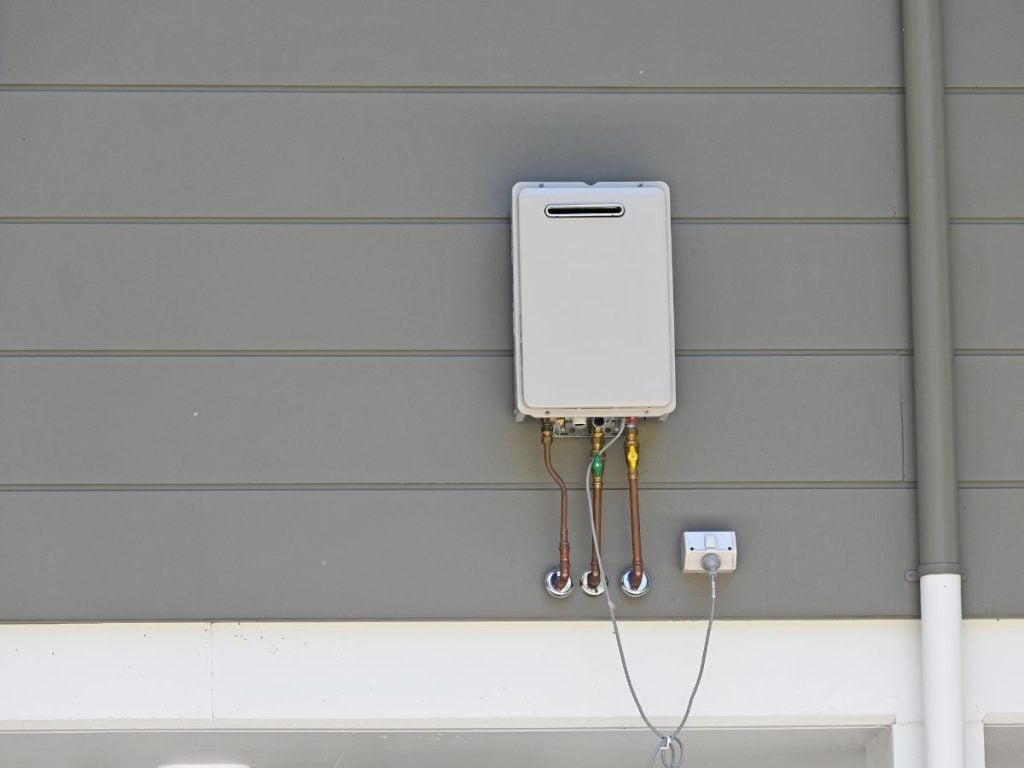 Hot Water Installation and Maintenance Mayfield » Mayfield A wide view of a grey tankless outdoor water heater mounted to a grey siding wall.