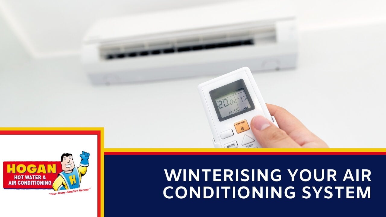 A hand pointing a remote control at a wall-mounted mini-split air conditioning unit.
