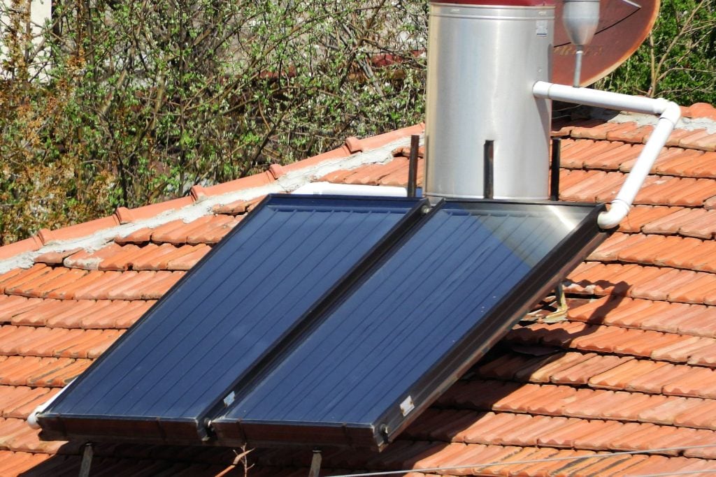 A solar water heater system with two flat collector panels and a cylindrical storage tank installed on a terracotta tiled roof.