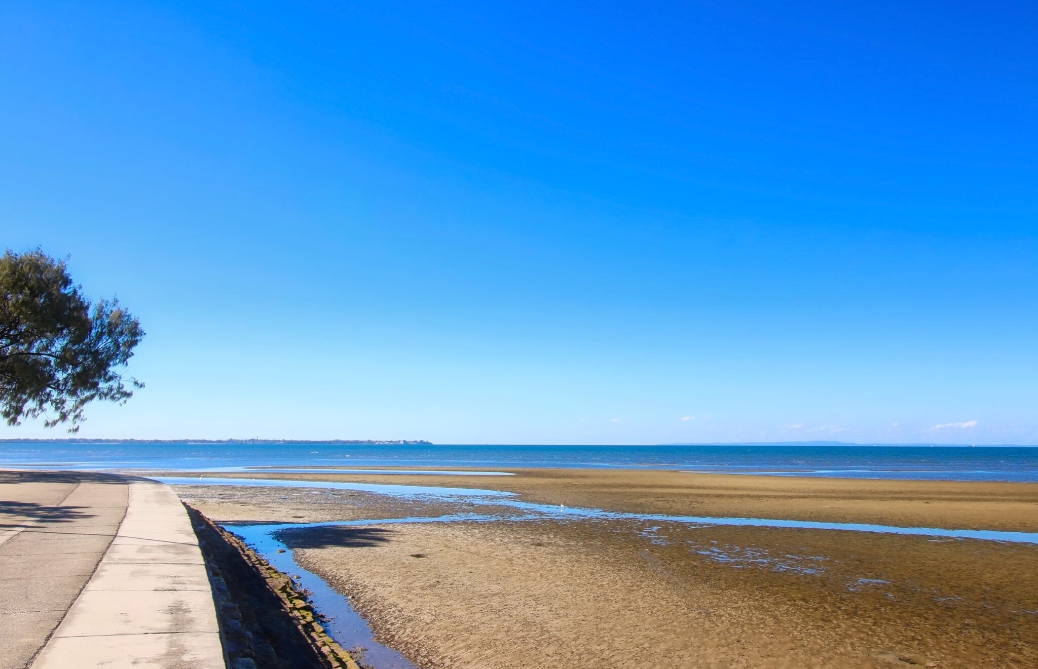 A coastal walkway bordering a sandy beach at low tide