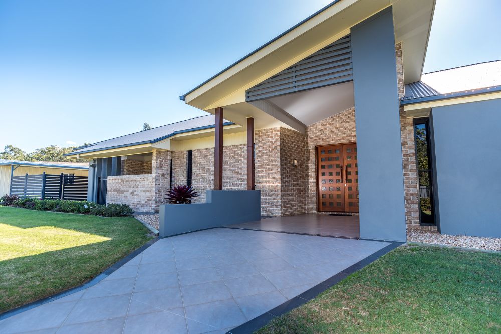 Chromagen Midea Heat Pumps » A modern brick and grey home with a tiled entryway leading to large double wooden doors under a prominent gabled roof.