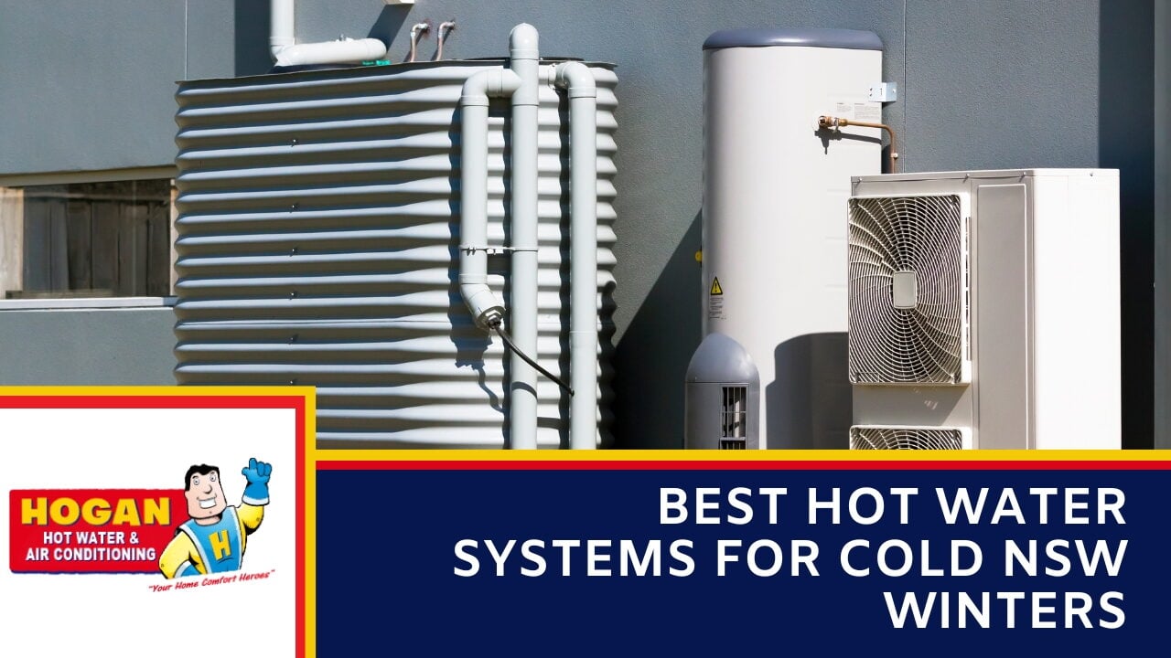 An outdoor hot water setup next to a grey building wall featuring a corrugated metal rainwater tank, a tall hot water storage cylinder, and a two-fan heat pump compressor unit.