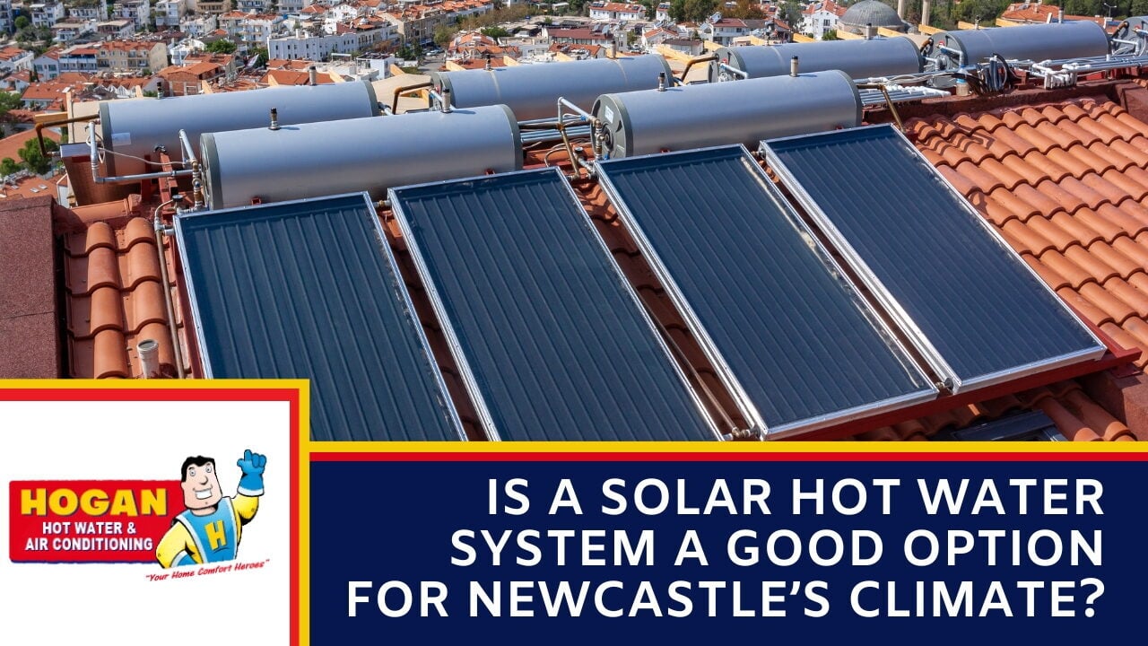 An array of four rooftop solar water heater panels with multiple grey storage tanks installed on a terracotta tile roof overlooking a town.