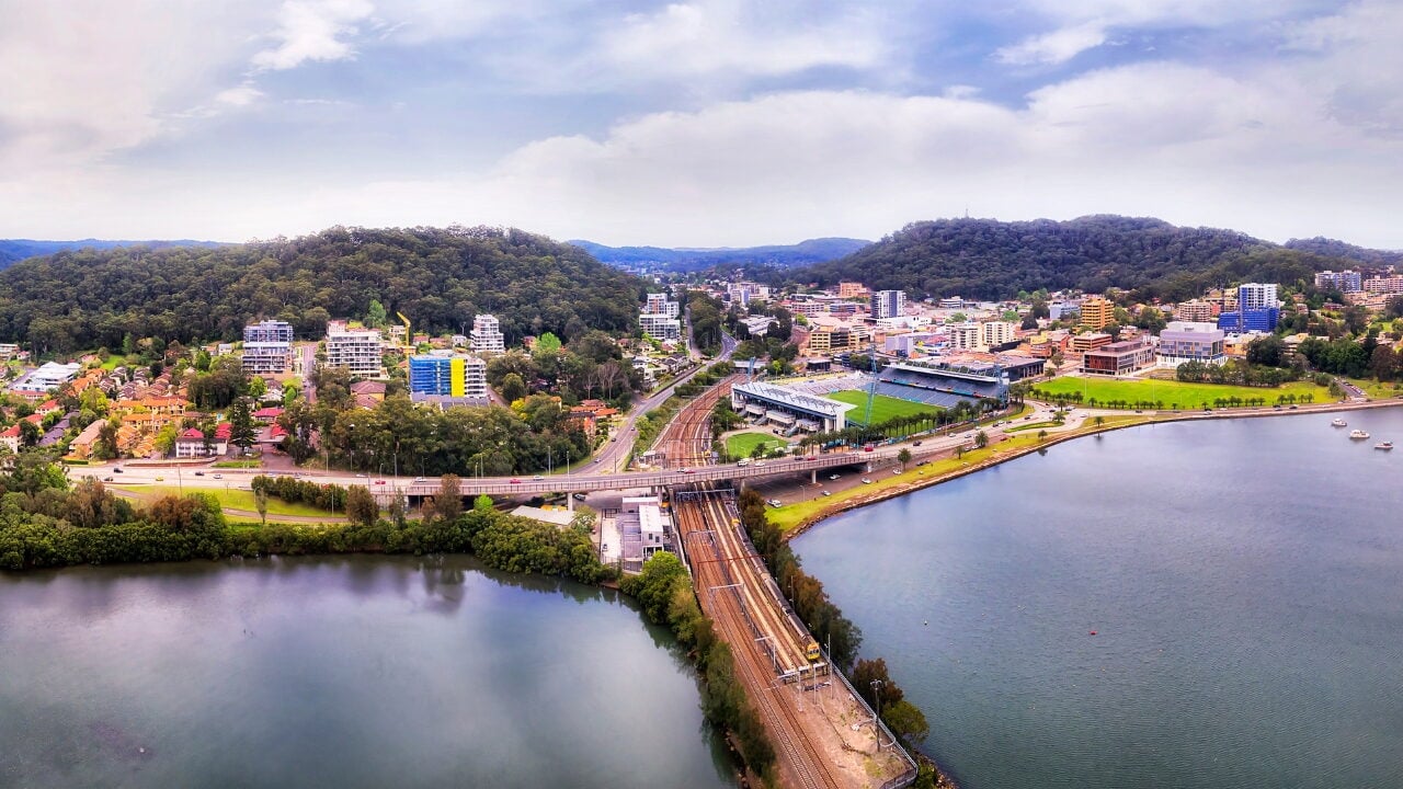 An aerial view of a coastal town featuring a railway line and highway bridge cutting across the water.