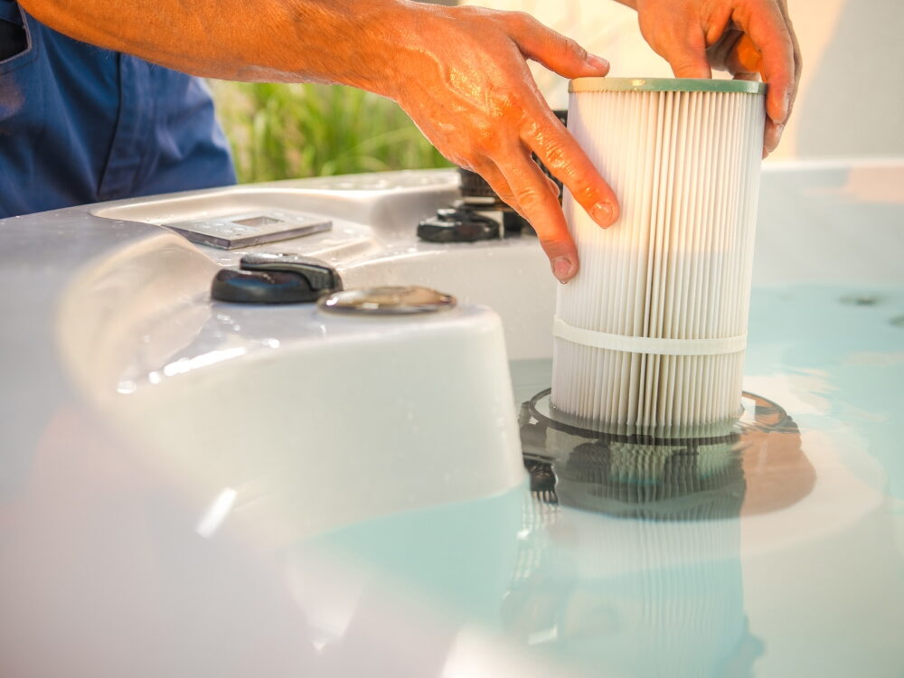 A close-up view of a person's hands installing or removing a cylindrical, pleated white cartridge filter.