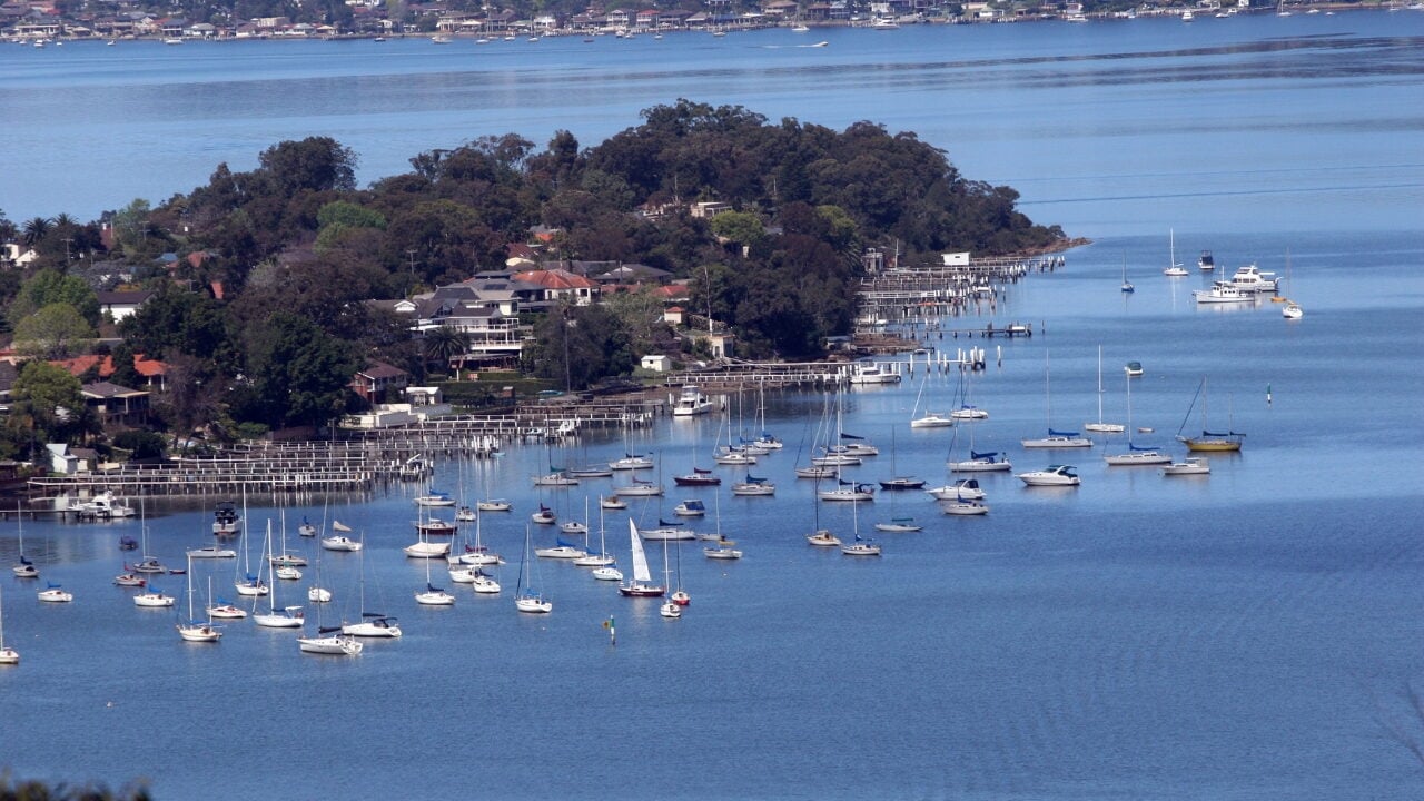 A calm blue bay filled with numerous anchored sailboats and small motorboats in Point Frederick.