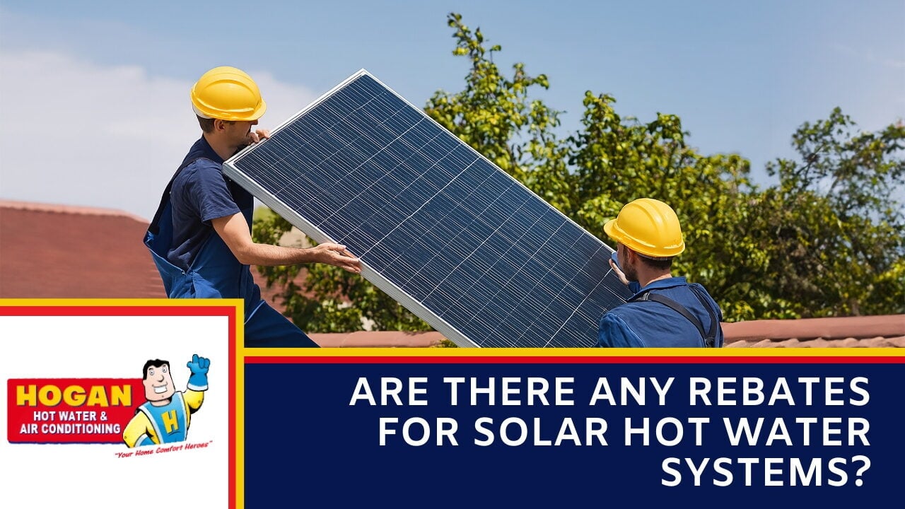 Two technicians wearing yellow hard hats and blue workwear carrying a large solar panel on a rooftop.