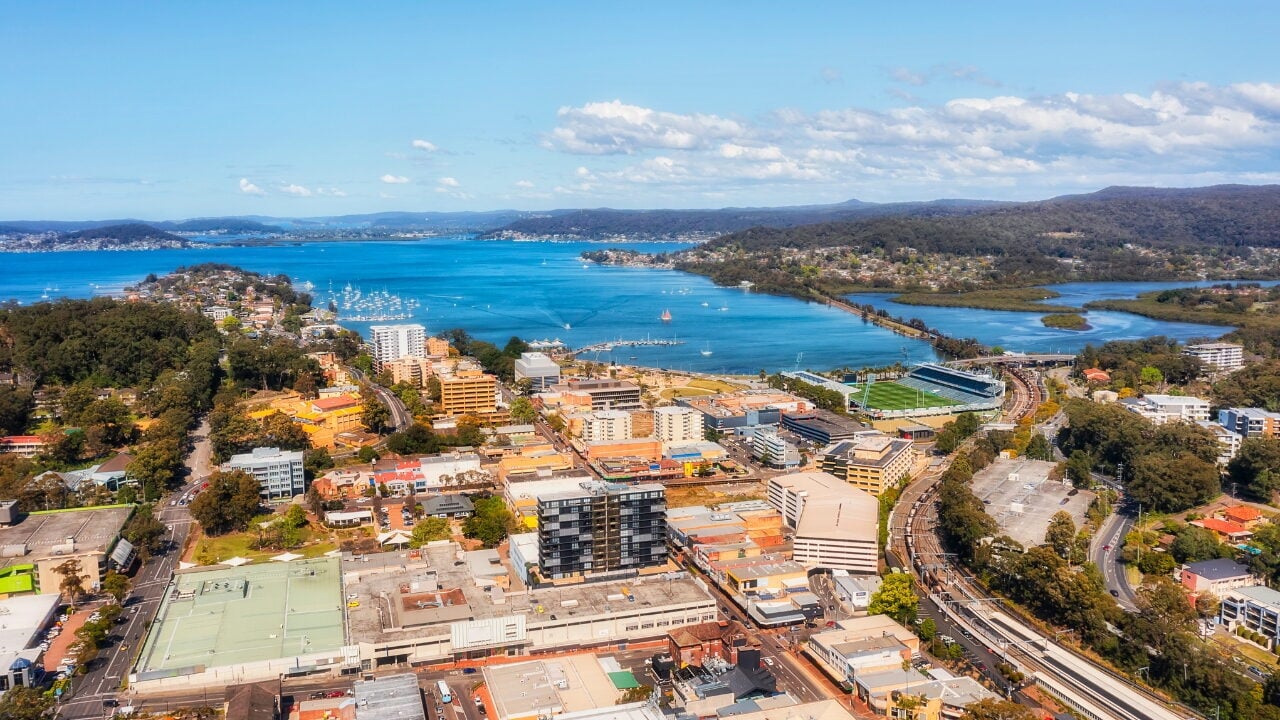 A coastal city with mid-rise buildings, a sports stadium, and a railway line running along the shore.