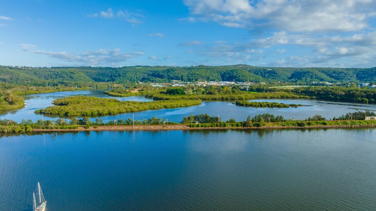 An aerial view of a wide blue river with green, marshy islands and a long, tree-lined thin strip of land cutting across the water.