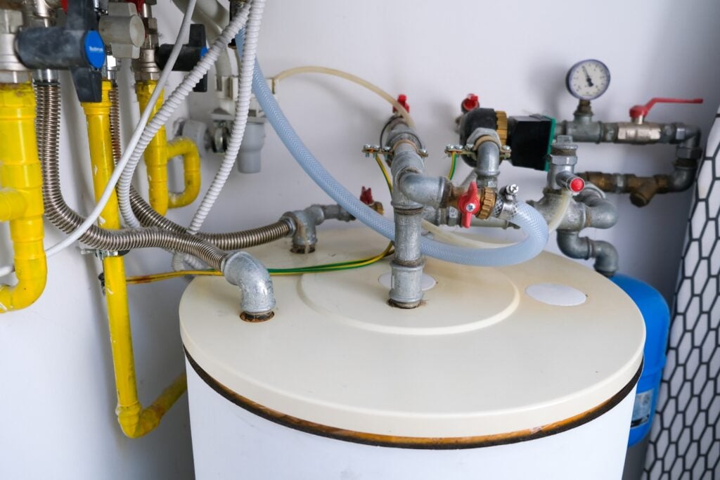 Hot Water Installation and Maintenance Phegans Bay » Hot Water A plumbing, metal pipes, yellow gas lines, flexible hoses, and valves connected to the top of a white domestic hot water storage tank.