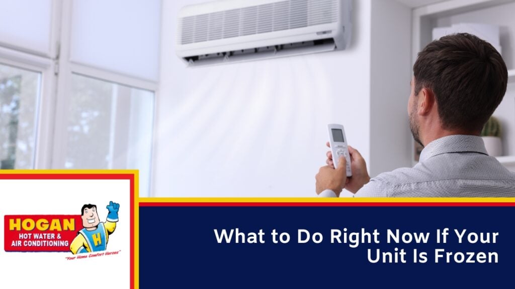 A man holds a remote control toward a wall-mounted split-system air conditioner in a bright room.