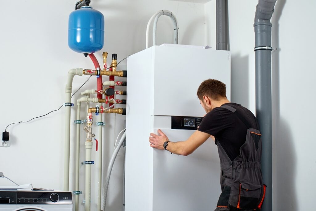 A technician troubleshoots a digital control panel of a white indoor heat pump system with pipes and expansion tank in Umina beach