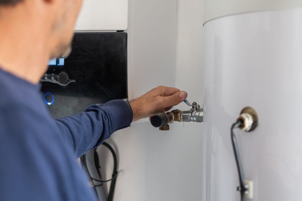 A technician adjusting a valve lever on a pipe connected to a large white water storage tank.