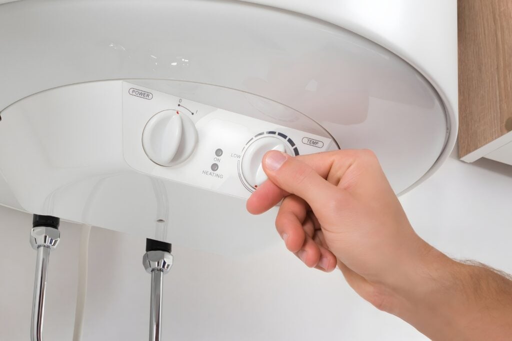 A close-up view of a person's hand turning a white temperature dial on the control panel of a wall-mounted hot water system.